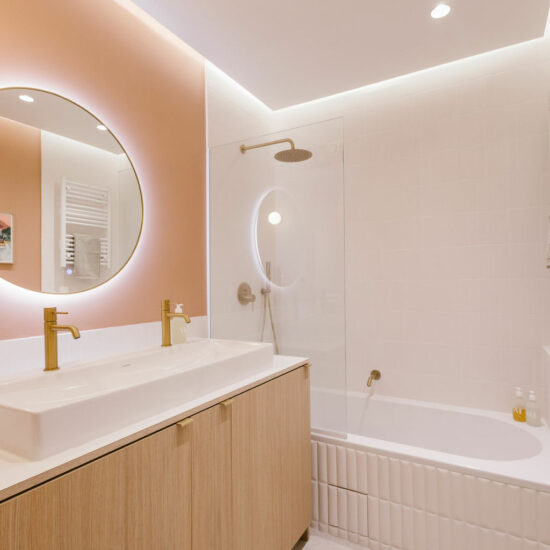 Salle de bain terracotta avec baignoire et meuble en bois strié. Robinetterie laiton et double vasque.
